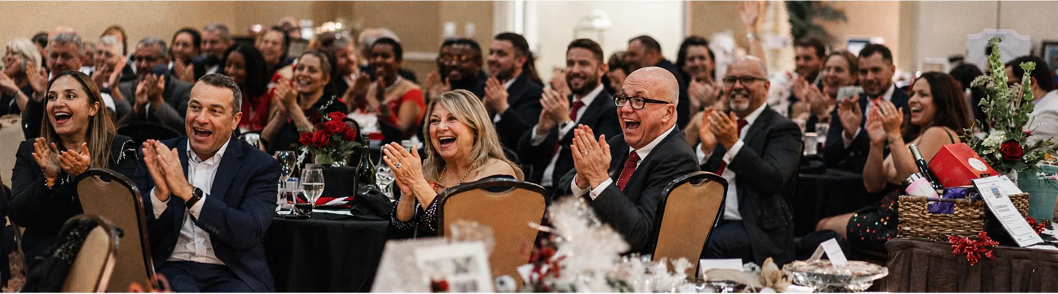 Guests at a gala laughing and applauding during a program run by a corporate emcee