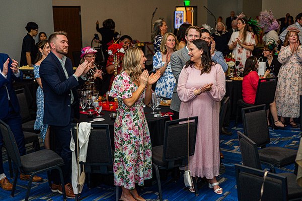 Guests standing and applauding between segments of a gala program run by a corporate emcee