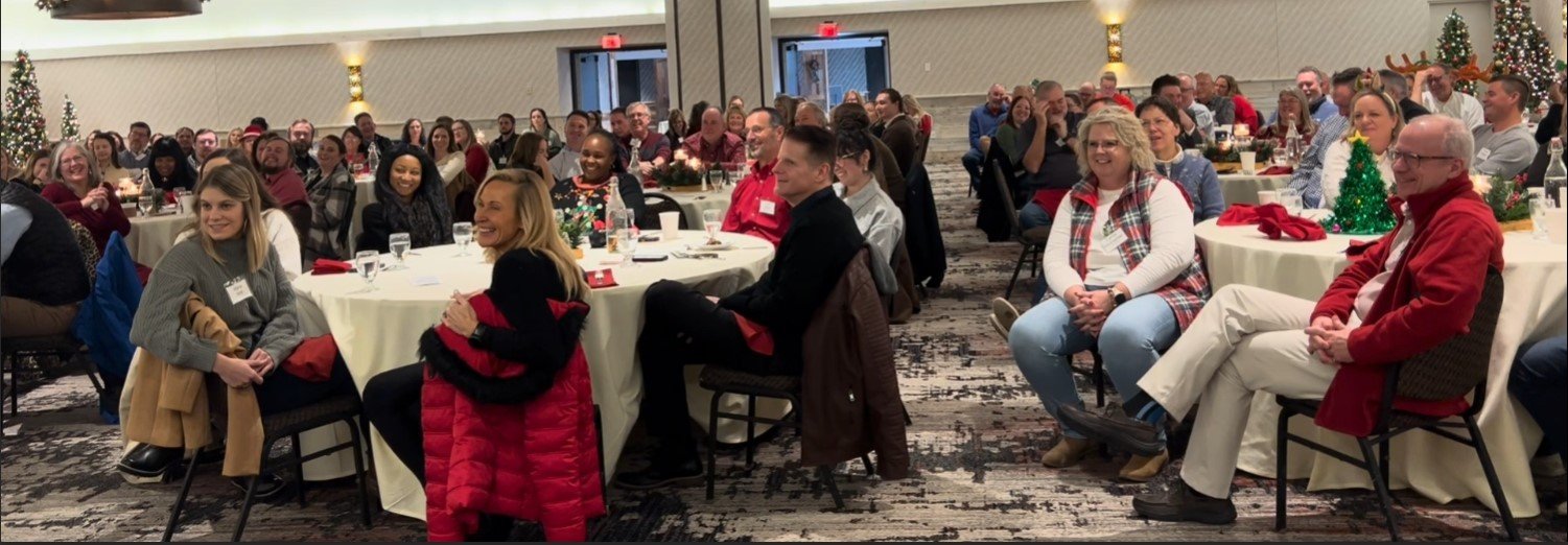 A full room of guests at a corporate holiday party watching a program run by their emcee